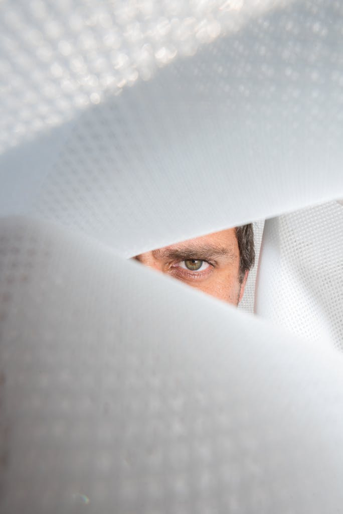 A single eye peers through an abstract white pattern evoking curiosity.